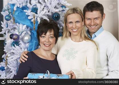 Senior woman and mid adult couple in front of Christmas tree, portrait