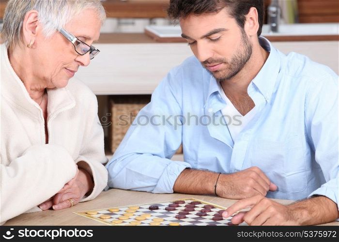 Senior woman and young man playing checkers