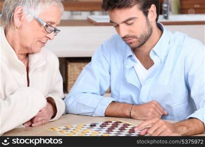 Senior woman and young man playing checkers