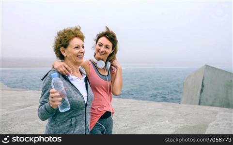 Senior woman and young woman walking outdoors by sea pier. Two women walking by sea pier