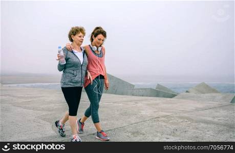 Senior woman and young woman walking outdoors by sea pier. Two women walking by sea pier