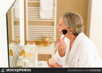 Senior woman apply make-up powder in front of bathroom mirror