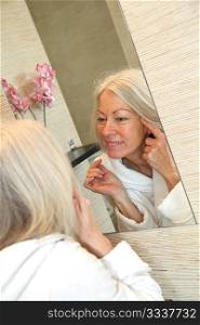 Senior woman applying moisturizer on her face