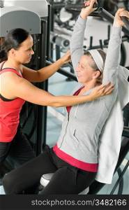 Senior woman at fitness center exercise on machine with trainer