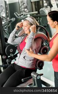 Senior woman at gym exercise with personal trainer on machine