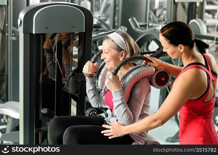 Senior woman at gym exercise with personal trainer on machine