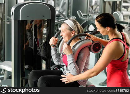 Senior woman at gym exercise with personal trainer on machine