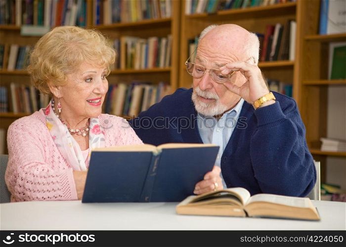 Senior woman at the library, showing her husband a passage in a book.