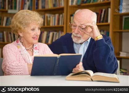 Senior woman at the library, showing her husband a passage in a book.