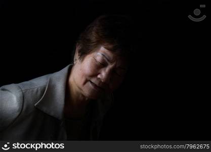Senior woman bending forward while displaying pain on black background.