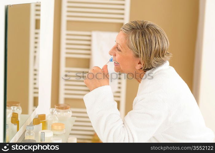 Senior woman brushing teeth in front of bathroom mirror