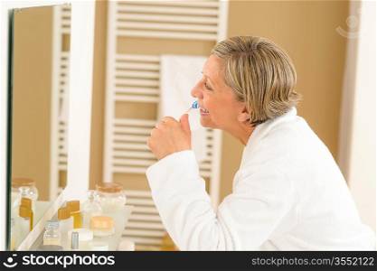 Senior woman brushing teeth in front of bathroom mirror