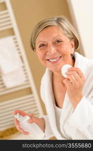 Senior woman clean face with cotton pad looking at camera