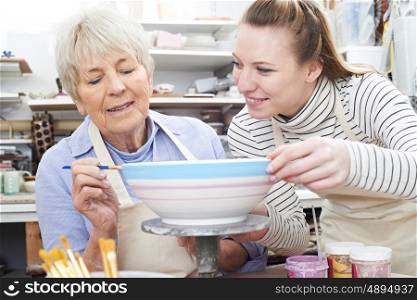 Senior Woman Decorating Bowl With Teacher In Pottery Class