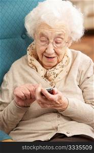 Senior Woman Dialling Number On Mobile Phone Sitting In Chair At Home