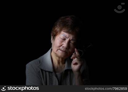 Senior woman displaying pain while holding reading glass on black background.