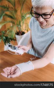 Senior Woman Doing Wrist Joint Physical Therapy with Conductive TENS Electrode Sock, Transcutaneous Electrical Nerve Stimulation. Senior Woman Doing Elbow Physical Therapy with TENS Electrode Brace Pads, Transcutaneous Electrical Nerve Stimulation