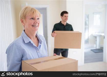 Senior Woman Downsizing In Retirement Carrying Boxes Into New Home On Moving Day With Removal Man Helping