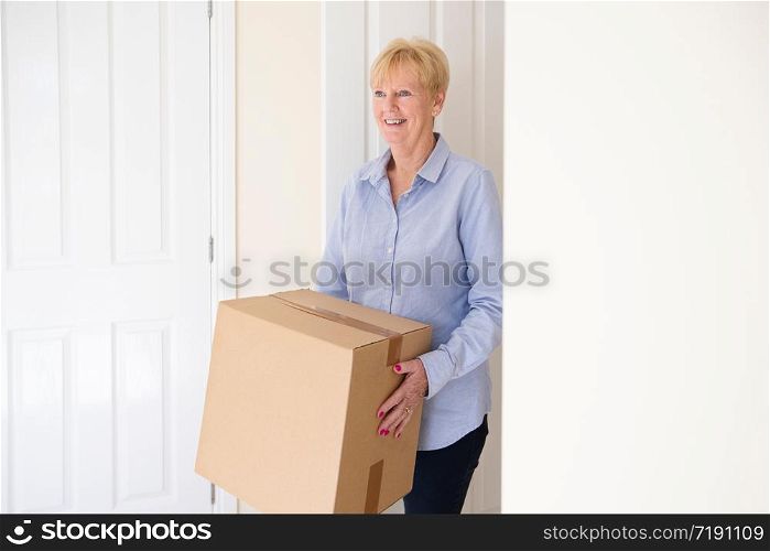 Senior Woman Downsizing In Retirement Carrying Boxes Into New Home On Moving Day