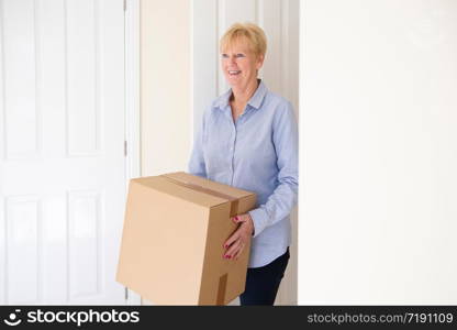 Senior Woman Downsizing In Retirement Carrying Boxes Into New Home On Moving Day