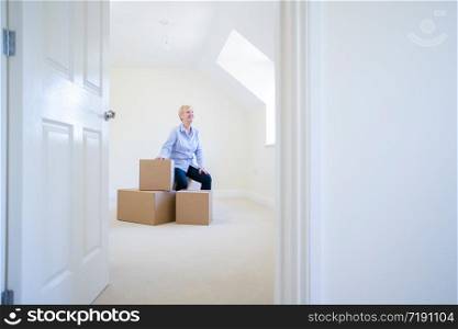 Senior Woman Downsizing In Retirement Sitting On Boxes In New Home On Moving Day