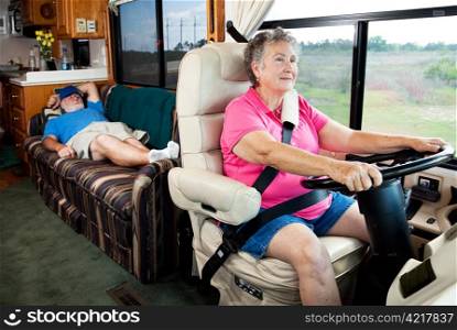 Senior woman driving the motor home on vacation while her husband sleeps in the back.