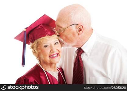 Senior woman earns a college degree and a kiss from her husband. Isolated on white.