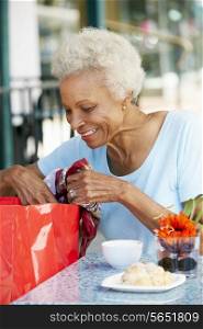 Senior Woman Enjoying Snack At Outdoor Cafe After Shopping