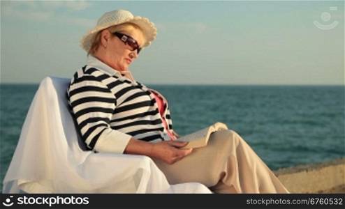 Senior woman enjoying vacation at the seaside, reading book. Medium shot