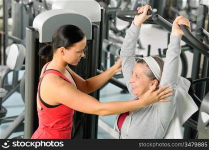 Senior woman exercise on shoulder press machine with personal trainer