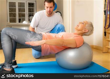 Senior woman exercising on Pilates ball with coach&rsquo;s help. Senior Woman Exercising on Pilates Ball