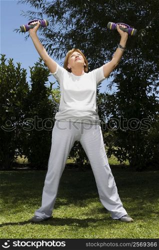 Senior woman exercising with dumbbells in a garden
