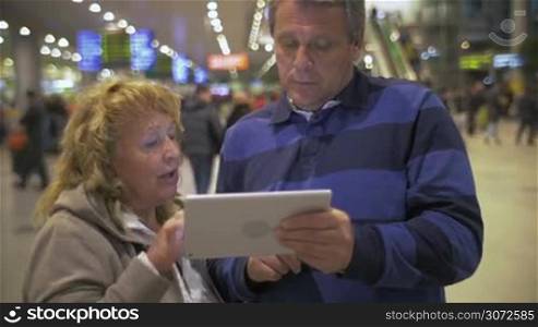 Senior woman explaining something to her husband using tablet computer at the airport
