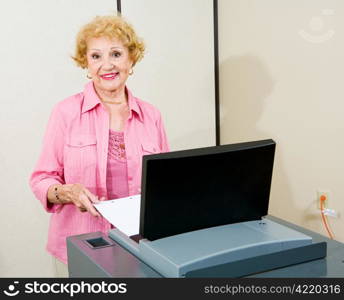 Senior woman feeding her ballot into a new optical scan voting machine. Authentic image shot at supervisor of elections.