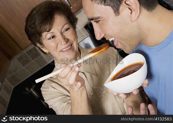 Senior woman feeding tomato soup to her son in the kitchen