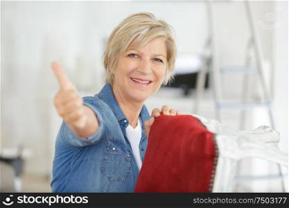 senior woman giving thumbs up while re-upholstering chair