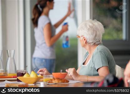 senior woman having breakfast with home care in the background