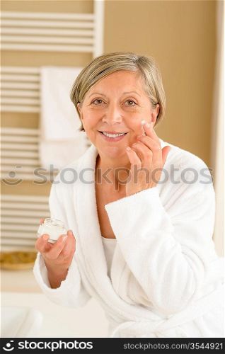 Senior woman hold anti-wrinkles cream in bathroom looking at camera