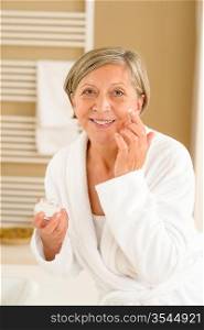 Senior woman hold anti-wrinkles cream in bathroom looking at camera