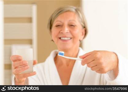 Senior woman hold toothbrush with toothpaste and glass of water