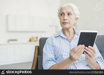 senior woman holding digital tablet looking away
