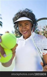 Senior woman holding tennis racket and balls, portrait