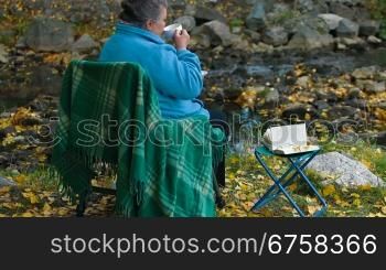 senior woman holding white coffee cup while sitting at autumn park