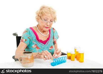 Senior woman in a wheelchair, couting out her pills for the week. White background.