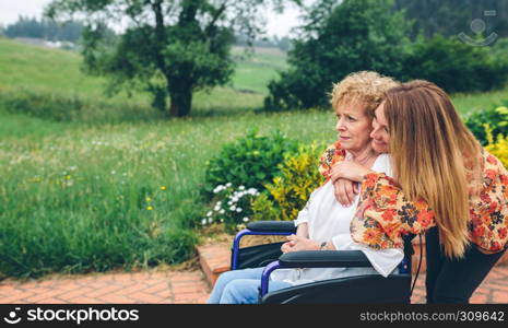 Senior woman in a wheelchair with her daughter in the garden. Senior woman in a wheelchair with her daughter