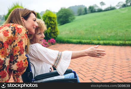 Senior woman in a wheelchair with her daughter looking at the landscape. Senior woman in a wheelchair with her daughter