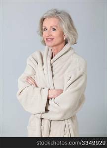 Senior woman in bathrobe standing on white background