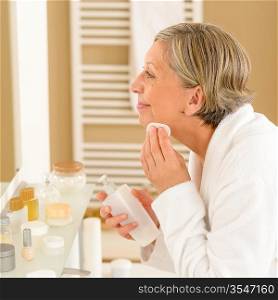 Senior woman in bathroom clean face make-up removal looking mirror