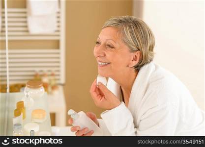 Senior woman in bathroom clean face with lotion and cotton pad