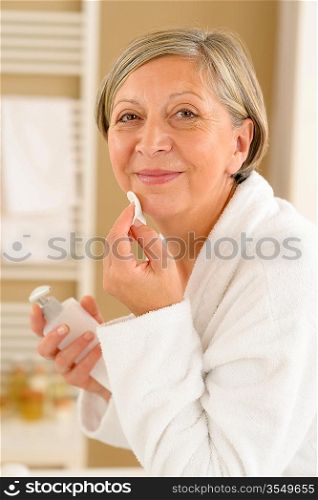 Senior woman in bathroom looking at camera cleaning facial cream